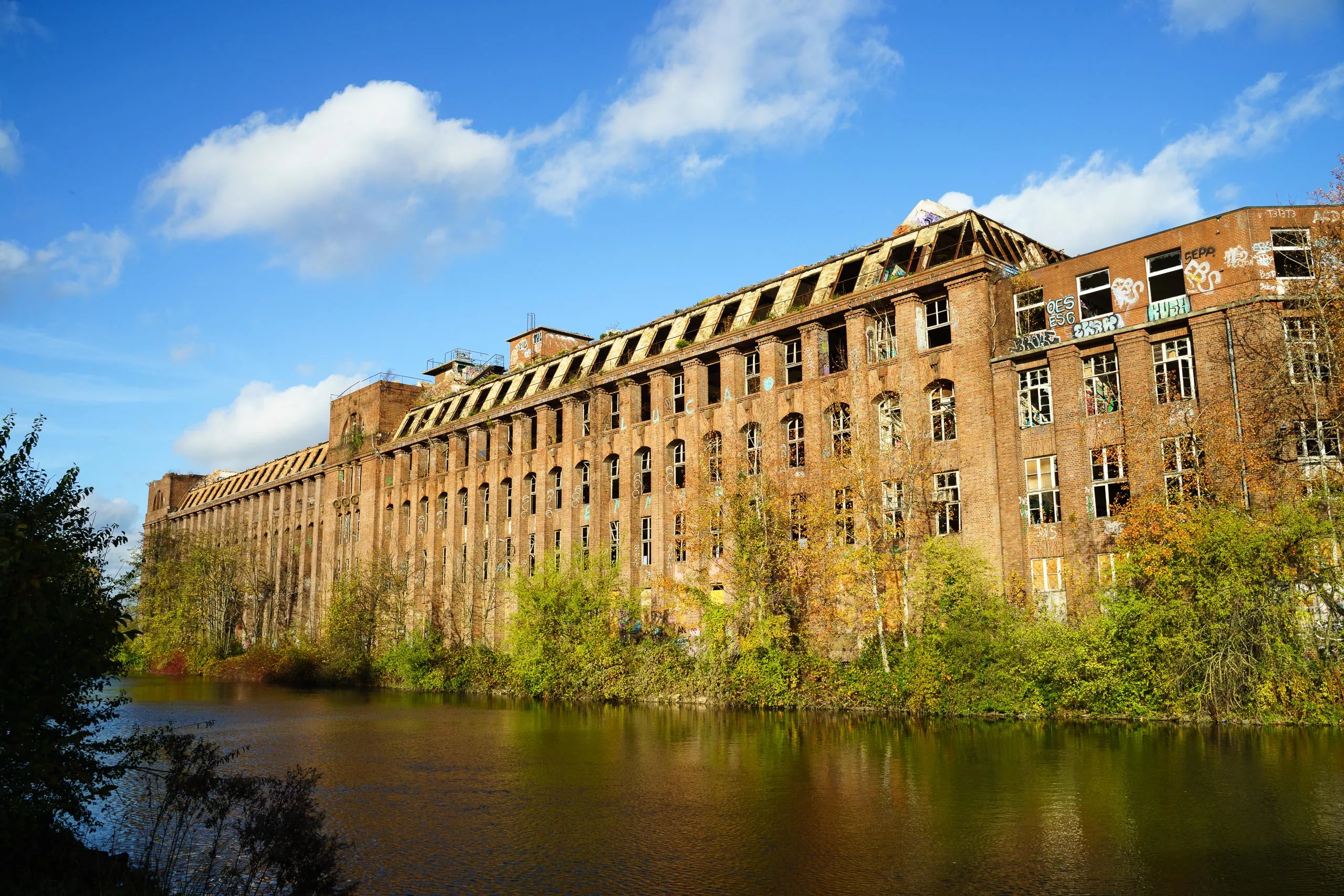 Alte Backsteinfassade des Continental-Werks am Wasser, mit offenen Fenstern und Bäumen am Ufer.